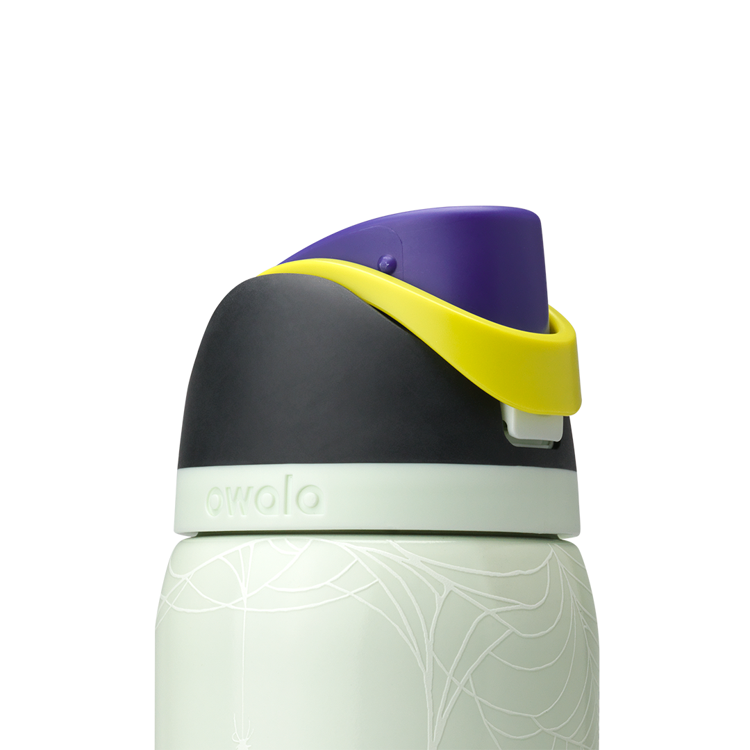 Owala FreeSip 32oz in RIP, lid detail showing dark charcoal flip cap closed, yellow carry loop, pale green accent ring on pale mint green body with skeleton-hand pattern; glows in the dark